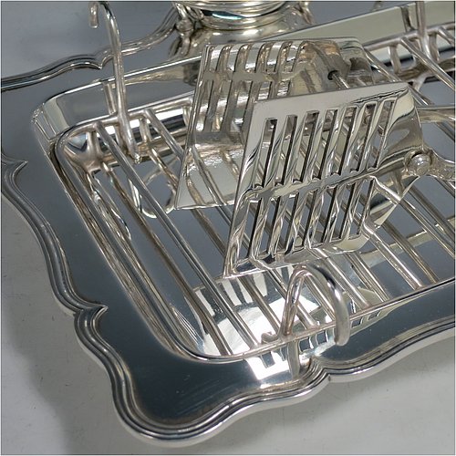 An Antique Edwardian Silver Plated asparagus serving set, having a plain rectangular body, with an applied and shaped reeded border, a wire-work serving rack, a sauce boat sat in a frame with loop handle, a pair of asparagus server tongs, and all sitting on a base with four button feet. All pieces were made by the Atkins Brothers of Sheffield in ca. 1900. The dimensions of this fine hand-made silver-plated asparagus serving set are length 29 cms (11.5 inches), and width, 23 cms (9 inches).    