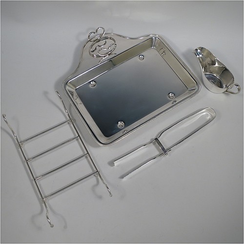 An Antique Edwardian Silver Plated asparagus serving set, having a plain rectangular body, with an applied gadroon border, a wire-work serving rack, a sauce boat sat in a frame with loop handle, a pair of asparagus server tongs, and all sitting on a base with four cast trefoil feet. All pieces were made by Mappin and Webb of London in ca. 1900. The dimensions of this fine hand-made antique silver-plated asparagus serving set are length 26.5 cms (10.5 inches), and width, 25.5 cms (10 inches).