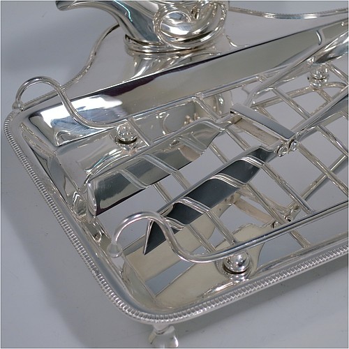 An Antique Edwardian Silver Plated asparagus serving set, having a plain rectangular body, with an applied gadroon border, a wire-work serving rack, a sauce boat sat in a frame with loop handle, a pair of asparagus server tongs, and all sitting on a base with four cast trefoil feet. All pieces were made by Mappin and Webb of London in ca. 1900. The dimensions of this fine hand-made antique silver-plated asparagus serving set are length 26.5 cms (10.5 inches), and width, 25.5 cms (10 inches).
