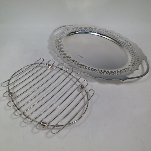 A pretty Antique Victorian Sterling Silver asparagus serving set, having a shaped oval body with cut out handles, a hand-cut Chippendale outer border with hand-pierced inner border of geometrical decoration, an original wire-work serving rack with four ball feet, and all sitting on a base with four cushion feet. Made by William Hutton and Sons of Sheffield in 1900. The dimensions of this fine hand-made antique silver asparagus serving set are length 35 cms (13.75 inches), and width 23.5 cms (9.25 inches), and with a total weight of approx. 925g (30 troy ounces).
