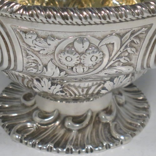 An Antique Victorian Sterling Silver sweet-meat basket, having a round baluster body with gold-gilt interior and an applied gadroon border, with hand-chased floral decoration between four round vacant cartouches, a hinged and florally chased swing handle, and all sitting on a swirl-fluted pedestal foot. Made by Martin and Hall of London in 1871. The dimensions of this fine hand-made antique silver basket are height 15 cms (6 inches), diameter 12.5 cms (5 inches), and it weighs approx. 224g (7.2 troy ounces).