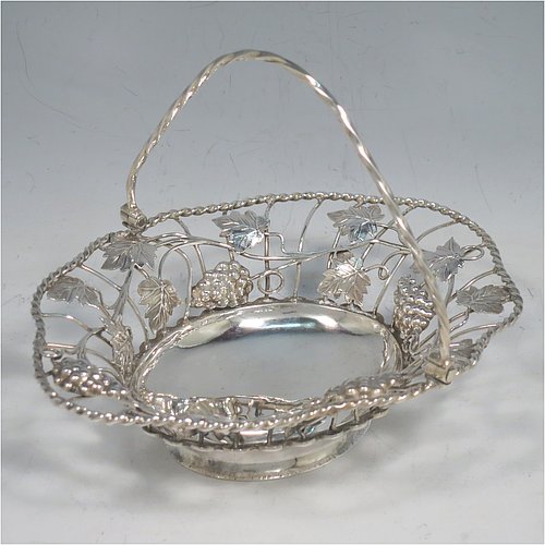 An Antique Georgian Sterling Silver sweet-meat basket with swing-handle, having wire-work decoration with applied grape-vines and leaves, a shaped rope-twist border, a hinged twisted handle, and all sitting on a plain collet foot. Made by Edward Aldridge of London in 1760. The dimensions of this fine hand-made antique silver sweetmeat basket are length 16 cms (6.3 inches), width 13 cms (5 inches), height 13 cms (5 inches), and it weighs approx. 155g (5 troy ounces).   