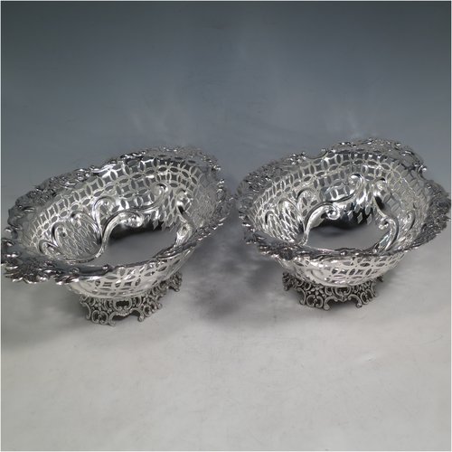 An Antique Edwardian pair of Sterling silver table baskets, having oval bodies with hand-pierced scroll-work decoration, with hand-chased floral borders, and sitting on matching pierced & scroll feet. Made by Charles Boyton of London in 1902. The dimensions of this fine pair of antique silver baskets are length 27 cms (10.75 inches), width 18.5 cms (7.25 inches), height 9 cms (3.5 inches), and they weigh a total of approx. 586g (19 troy ounces).   