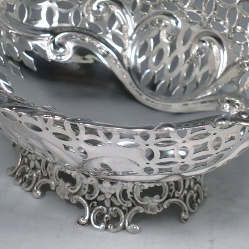 An Antique Edwardian pair of Sterling silver table baskets, having oval bodies with hand-pierced scroll-work decoration, with hand-chased floral borders, and sitting on matching pierced & scroll feet. Made by Charles Boyton of London in 1902. The dimensions of this fine pair of antique silver baskets are length 27 cms (10.75 inches), width 18.5 cms (7.25 inches), height 9 cms (3.5 inches), and they weigh a total of approx. 586g (19 troy ounces).