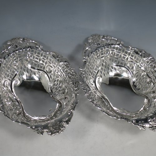 An Antique Edwardian pair of Sterling silver table baskets, having oval bodies with hand-pierced scroll-work decoration, with hand-chased floral borders, and sitting on matching pierced & scroll feet. Made by Charles Boyton of London in 1902. The dimensions of this fine pair of antique silver baskets are length 27 cms (10.75 inches), width 18.5 cms (7.25 inches), height 9 cms (3.5 inches), and they weigh a total of approx. 586g (19 troy ounces).