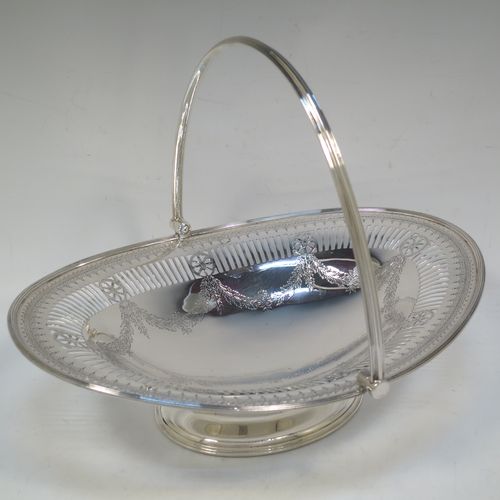 A very pretty Antique Victorian Sterling Silver basket, having an oval body with an applied reeded border, all hand-engraved in a neoclassical style with swags of floral decoration below an upper band of hand-piercing, a hinged and reeded swing handle, and all sitting on an oval pedestal foot. Made in Sheffield in 1879. The dimensions of this fine hand-made antique silver basket are height 21.5 cms (8.5 inches), length 28 cms (11 inches), width 23 cms (9 inches), and it weighs approx. 495g (16 troy ounces).   