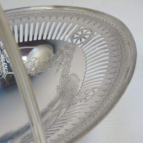 A very pretty Antique Victorian Sterling Silver basket, having an oval body with an applied reeded border, all hand-engraved in a neoclassical style with swags of floral decoration below an upper band of hand-piercing, a hinged and reeded swing handle, and all sitting on an oval pedestal foot. Made in Sheffield in 1879. The dimensions of this fine hand-made antique silver basket are height 21.5 cms (8.5 inches), length 28 cms (11 inches), width 23 cms (9 inches), and it weighs approx. 495g (16 troy ounces).