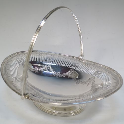 A very pretty Antique Victorian Sterling Silver basket, having an oval body with an applied reeded border, all hand-engraved in a neoclassical style with swags of floral decoration below an upper band of hand-piercing, a hinged and reeded swing handle, and all sitting on an oval pedestal foot. Made in Sheffield in 1879. The dimensions of this fine hand-made antique silver basket are height 21.5 cms (8.5 inches), length 28 cms (11 inches), width 23 cms (9 inches), and it weighs approx. 495g (16 troy ounces).