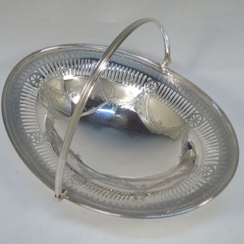 A very pretty Antique Victorian Sterling Silver basket, having an oval body with an applied reeded border, all hand-engraved in a neoclassical style with swags of floral decoration below an upper band of hand-piercing, a hinged and reeded swing handle, and all sitting on an oval pedestal foot. Made in Sheffield in 1879. The dimensions of this fine hand-made antique silver basket are height 21.5 cms (8.5 inches), length 28 cms (11 inches), width 23 cms (9 inches), and it weighs approx. 495g (16 troy ounces).
