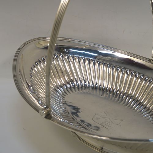 A very handsome Antique Georgian Sterling Silver basket, having an oval body with an applied reeded border, with hand-chased fluted decoration, a hinged and reeded swing handle, all sitting on a plain oval collet foot. This elegant antique silver basket was made by Joseph Scammell of London in 1795. The dimensions of this fine hand-made antique silver basket are height 28 cms (11 inches), length 37 cms (14.5 inches), width 26 cms (10.25 inches), and it weighs approx. 899g (29 troy ounces). Please note that this basket is crested.