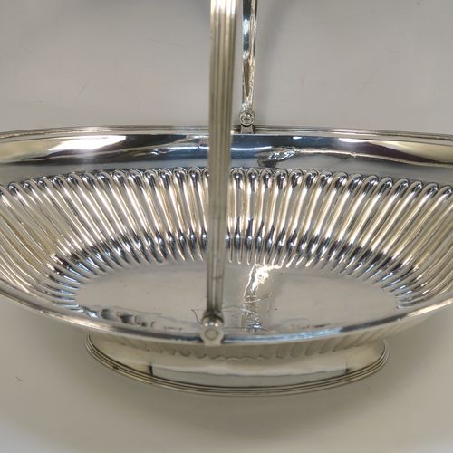 A very handsome Antique Georgian Sterling Silver basket, having an oval body with an applied reeded border, with hand-chased fluted decoration, a hinged and reeded swing handle, all sitting on a plain oval collet foot. This elegant antique silver basket was made by Joseph Scammell of London in 1795. The dimensions of this fine hand-made antique silver basket are height 28 cms (11 inches), length 37 cms (14.5 inches), width 26 cms (10.25 inches), and it weighs approx. 899g (29 troy ounces). Please note that this basket is crested.