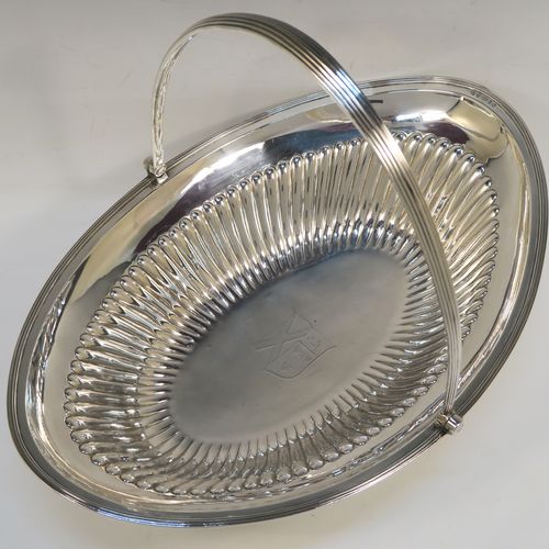 A very handsome Antique Georgian Sterling Silver basket, having an oval body with an applied reeded border, with hand-chased fluted decoration, a hinged and reeded swing handle, all sitting on a plain oval collet foot. This elegant antique silver basket was made by Joseph Scammell of London in 1795. The dimensions of this fine hand-made antique silver basket are height 28 cms (11 inches), length 37 cms (14.5 inches), width 26 cms (10.25 inches), and it weighs approx. 899g (29 troy ounces). Please note that this basket is crested.