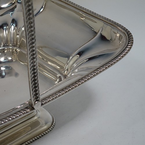 An Antique Edwardian Sterling Silver basket, having a rectangular body, with an applied gadroon border, a hinged and swing handle with gadroon edges, all sitting on a pedestal foot. Made by the Dixon Brothers of Sheffield in 1910. The dimensions of this fine hand-made antique silver basket are height 23 cms (9 inches), length 27.5 cms (10.75 inches), width 21 cms (8.25 inches), and it weighs approx. 746g (24 troy ounces).