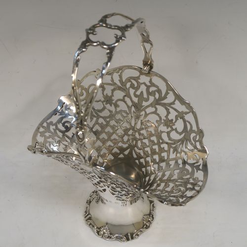 A very pretty Antique Edwardian Sterling Silver wedding style basket, having an oval body with applied scroll borders and hand-pierced floral and geometrical decoration, and a matching swing handle, all sitting on a pedestal foot. This beautiful silver wedding basket was made in Birmingham in 1910. The dimensions of this fine hand-made antique silver wedding basket are height 23 cms (9 inches), length 15 cms (6 inches), width 11.5 cms (4.5 inches), and it weighs approx. 243g (7.8 troy ounces).