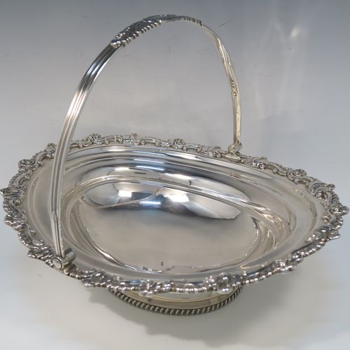 A handsome Antique Georgian Regency style sterling silver basket, having a plain bellied oval body, with an applied shell and scroll border, a hinged and swing handle, all sitting on an oval pedestal foot with an applied gadroon border. This elegant antique silver basket was made by S. C. Younge and Co., of Sheffield in 1815. The dimensions of this fine hand-made Regency silver basket are height 25 cms (10 inches), length 33 cms (13 inches), width 28 cms (11 inches), and it weighs approx. 1,189g (38 troy ounces).   