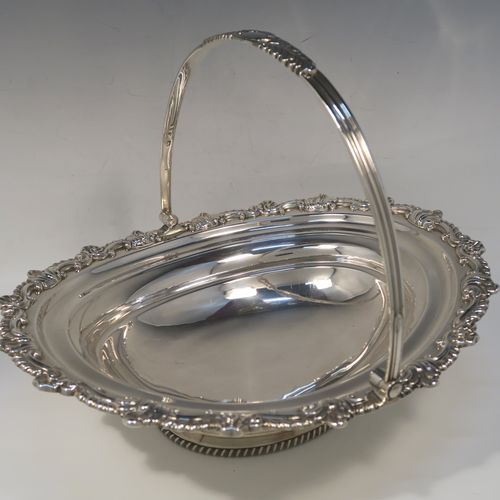 A handsome Antique Georgian Regency style sterling silver basket, having a plain bellied oval body, with an applied shell and scroll border, a hinged and swing handle, all sitting on an oval pedestal foot with an applied gadroon border. This elegant antique silver basket was made by S. C. Younge and Co., of Sheffield in 1815. The dimensions of this fine hand-made Regency silver basket are height 25 cms (10 inches), length 33 cms (13 inches), width 28 cms (11 inches), and it weighs approx. 1,189g (38 troy ounces).   