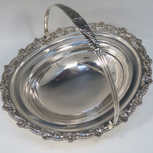 A handsome Antique Georgian Regency style sterling silver basket, having a plain bellied oval body, with an applied shell and scroll border, a hinged and swing handle, all sitting on an oval pedestal foot with an applied gadroon border. This elegant antique silver basket was made by S. C. Younge and Co., of Sheffield in 1815. The dimensions of this fine hand-made Regency silver basket are height 25 cms (10 inches), length 33 cms (13 inches), width 28 cms (11 inches), and it weighs approx. 1,189g (38 troy ounces).   