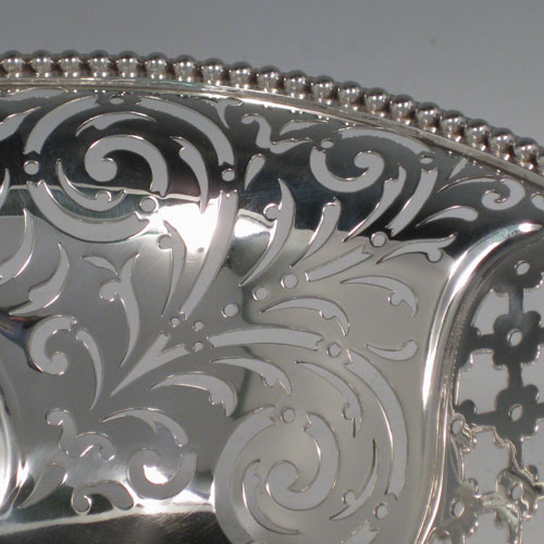 Antique Victorian sterling silver bread / fruit basket, having an oval body with hand-pierced geometrical and floral decoration, an applied cast bead border, two cast and hinged side-handles, and all sitting on a pedestal foot. Made by Edward and John Barnard of London in 1862. Length 34 cms (13.5 inches), width 26.5 cms (10.5 inches), height 11.5 cms (4.5 inches). Weight approx. 1,099g (35.5 troy ounces).
