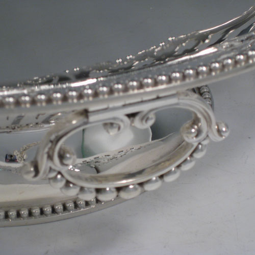 Antique Victorian sterling silver bread / fruit basket, having an oval body with hand-pierced geometrical and floral decoration, an applied cast bead border, two cast and hinged side-handles, and all sitting on a pedestal foot. Made by Edward and John Barnard of London in 1862. Length 34 cms (13.5 inches), width 26.5 cms (10.5 inches), height 11.5 cms (4.5 inches). Weight approx. 1,099g (35.5 troy ounces).