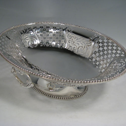Antique Victorian sterling silver bread / fruit basket, having an oval body with hand-pierced geometrical and floral decoration, an applied cast bead border, two cast and hinged side-handles, and all sitting on a pedestal foot. Made by Edward and John Barnard of London in 1862. Length 34 cms (13.5 inches), width 26.5 cms (10.5 inches), height 11.5 cms (4.5 inches). Weight approx. 1,099g (35.5 troy ounces).
