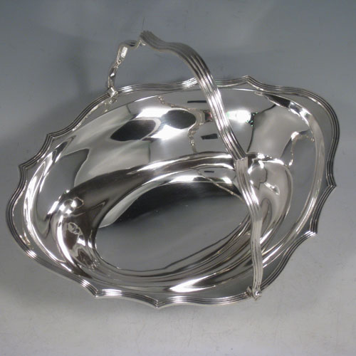 An elegant Antique Edwardian Sterling Silver table basket, having a plain oval body with shaped border and applied reeded edge, a hinged reeded handle, and sitting on a collet foot with reeded border. This handsome silver basket was made by Charles Stuart Harris of London in 1903. The dimensions of this fine hand-made antique silver basket are height inc. handle 20 cms (8 inches), length 23 cms (9 inches), 19 cms (7.5 inches), and it weighs approx. 339g (11 troy ounces).