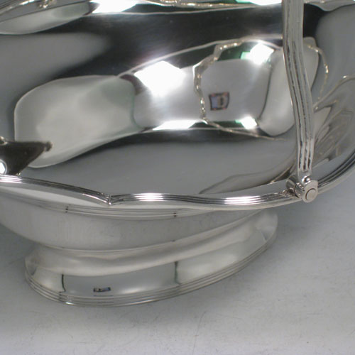 An elegant Antique Edwardian Sterling Silver table basket, having a plain oval body with shaped border and applied reeded edge, a hinged reeded handle, and sitting on a collet foot with reeded border. This handsome silver basket was made by Charles Stuart Harris of London in 1903. The dimensions of this fine hand-made antique silver basket are height inc. handle 20 cms (8 inches), length 23 cms (9 inches), 19 cms (7.5 inches), and it weighs approx. 339g (11 troy ounces).