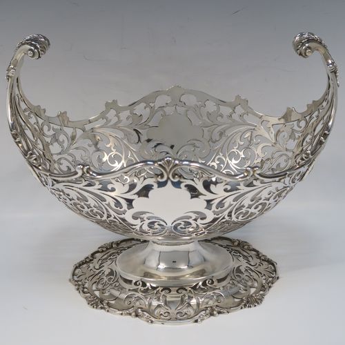 A large and very pretty Antique Sterling silver fruit basket, having an oval body with hand-pierced floral and scroll decoration, applied cast scroll and floral borders, with two cast scroll and shell flying side-handles, and all sitting on a matching pedestal foot. This beautiful antique silver basket was made by Jackson and Fullerton of London in 1912. The dimensions of this fine antique silver basket are length 27 cms (10.5 inches), width 18 cms (7 inches), height 22 cms (8.75 inches), and it weighs approx. 1,062g (34 troy ounces).   