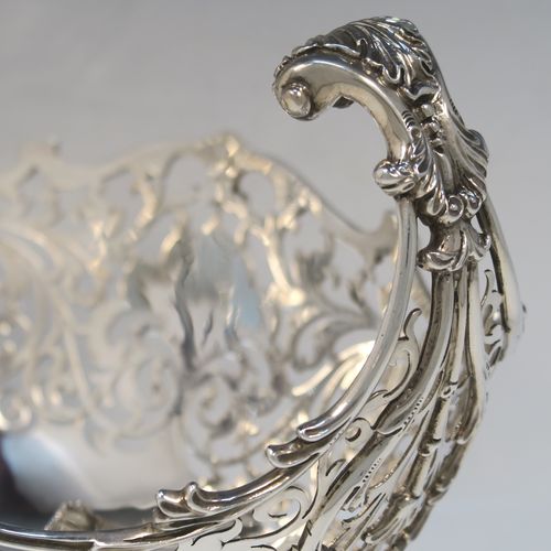 A large and very pretty Antique Sterling silver fruit basket, having an oval body with hand-pierced floral and scroll decoration, applied cast scroll and floral borders, with two cast scroll and shell flying side-handles, and all sitting on a matching pedestal foot. This beautiful antique silver basket was made by Jackson and Fullerton of London in 1912. The dimensions of this fine antique silver basket are length 27 cms (10.5 inches), width 18 cms (7 inches), height 22 cms (8.75 inches), and it weighs approx. 1,062g (34 troy ounces).