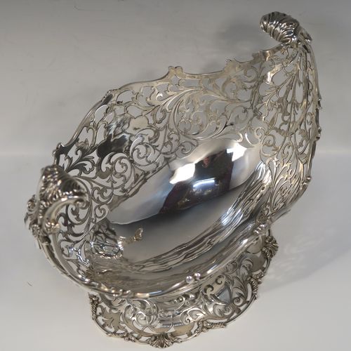 A large and very pretty Antique Sterling silver fruit basket, having an oval body with hand-pierced floral and scroll decoration, applied cast scroll and floral borders, with two cast scroll and shell flying side-handles, and all sitting on a matching pedestal foot. This beautiful antique silver basket was made by Jackson and Fullerton of London in 1912. The dimensions of this fine antique silver basket are length 27 cms (10.5 inches), width 18 cms (7 inches), height 22 cms (8.75 inches), and it weighs approx. 1,062g (34 troy ounces).