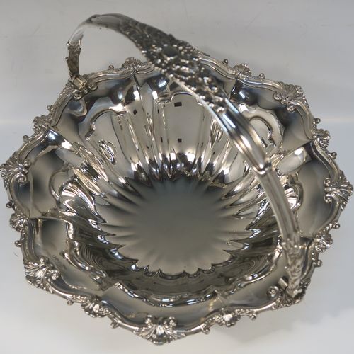 A very pretty Antique Victorian Silver-Plated basket, having a round body with hand-chased fluted decoration and an applied shell and scroll border, a hinged swing handle with applied floral decoration, and all sitting on a round fluted pedestal foot. This beautiful silver-plated swing-handle basket was made by Walker and Hall of Sheffield in ca. 1880. The dimensions of this fine hand-made antique silver-plated basket are height (inc. handles) 25.5 cms (10 inches), and diameter  28 cms (11 inches),   