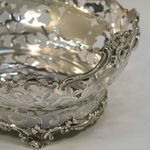 A very pretty Antique Scottish Edwardian Sterling silver small fruit basket, having an oval body with hand-pierced and engraved floral and scroll decoration, applied cast scroll and floral borders, and all sitting on four cast foliate feet. This beautiful antique silver basket was made by Hamilton and Inches of Edinburgh in 1904. The dimensions of this fine antique silver basket are length 20 cms (8 inches), width 17 cms (6.75 inches), height 10 cms (4 inches), and it weighs approx. 452g (14.6 troy ounces).   