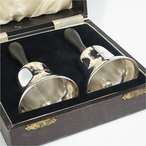 A Sterling Silver pair of Georgian style table bells, having plain round bellied bodies, with hand-turned wooden handles, and original silver clappers, all in their original cream satin and black velvet-lined presentation box. Made by Gladwin and Co., Ltd., of Sheffield in 1935. The dimensions of this fine hand-made pair of silver table bells are height 11.5 cms (4.5 inches), diameter at base 6.5 cms (2.5 inches), and they weigh a total of approx. 280g (9 troy ounces).   