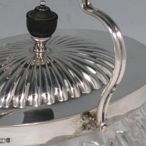 A very pretty Antique Victorian Sterling Silver and hand-cut crystal biscuit jar, having an unusual oval crystal body with hand-cut floral and geometric work, a lift-off lid with half-fluting and wooden finial, and a wire-work swing handle. Made by Fordham and Faulkner of Sheffield in 1901. The dimensions of this fine hand-made antique silver and crystal biscuit jar are height 18 cms (7 inches), length 20 cms (8 inches), and width 15 cms (6 inches).