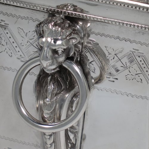 An Antique Victorian Silver Plated biscuit box, having a Neoclassical style rectangular shaped body with straight sides, applied bead-edged borders, with two bands of hand-engraving above and below a vacant cartouche, a hinged lid with ivory finial, two cast lion-mask ring handles, and all sitting on four cast lions-paw feet. Made in ca. 1880. The dimensions of this fine hand-made silver-plated biscuit boxr are height 18 cms (7 inches), length 21 cms (8.25 inches), and width 15 cms (6 inches).