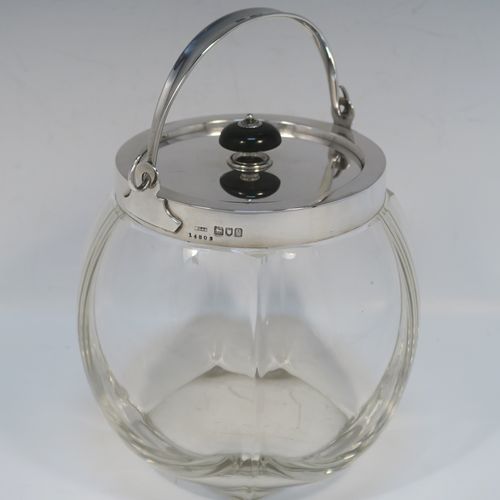 A handsome Antique Edwardian Sterling Silver and hand-cut crystal biscuit jar, having an unusual rounded crystal body with hand-cut panels, a plain round lift-off lid with a wooden finial, a swing handle attached to a plain round mount, and all sitting on a flat square base. This elegant silver and crystal biscuit jar was made by John Grinsell and Sons of London in 1902. The dimensions of this fine hand-made antique silver and crystal biscuit jar are height (excluding handle) 15 cms (6 inches), and diameter of main body 14 cms (5.5 inches).   