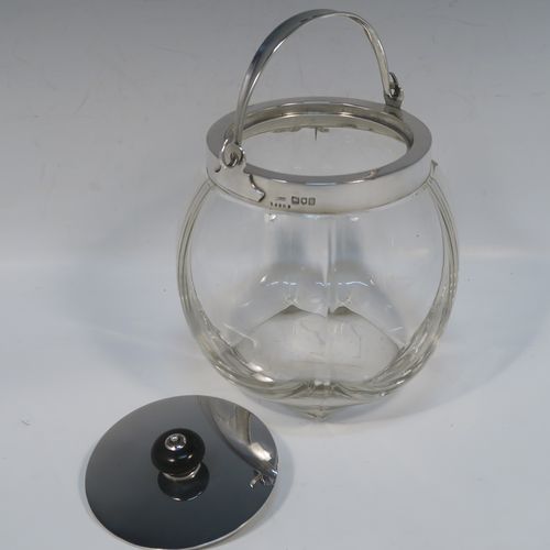 A handsome Antique Edwardian Sterling Silver and hand-cut crystal biscuit jar, having an unusual rounded crystal body with hand-cut panels, a plain round lift-off lid with a wooden finial, a swing handle attached to a plain round mount, and all sitting on a flat square base. This elegant silver and crystal biscuit jar was made by John Grinsell and Sons of London in 1902. The dimensions of this fine hand-made antique silver and crystal biscuit jar are height (excluding handle) 15 cms (6 inches), and diameter of main body 14 cms (5.5 inches).