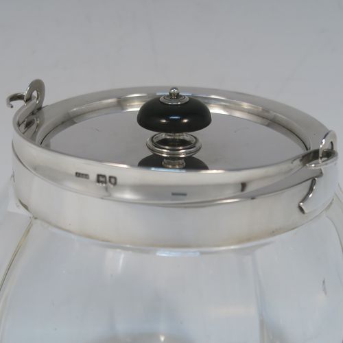 A handsome Antique Edwardian Sterling Silver and hand-cut crystal biscuit jar, having an unusual rounded crystal body with hand-cut panels, a plain round lift-off lid with a wooden finial, a swing handle attached to a plain round mount, and all sitting on a flat square base. This elegant silver and crystal biscuit jar was made by John Grinsell and Sons of London in 1902. The dimensions of this fine hand-made antique silver and crystal biscuit jar are height (excluding handle) 15 cms (6 inches), and diameter of main body 14 cms (5.5 inches).