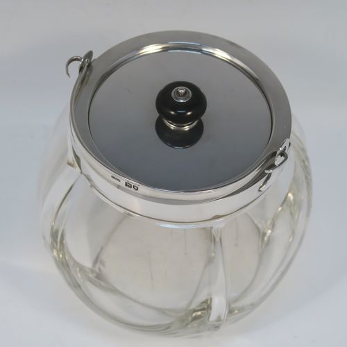 A handsome Antique Edwardian Sterling Silver and hand-cut crystal biscuit jar, having an unusual rounded crystal body with hand-cut panels, a plain round lift-off lid with a wooden finial, a swing handle attached to a plain round mount, and all sitting on a flat square base. This elegant silver and crystal biscuit jar was made by John Grinsell and Sons of London in 1902. The dimensions of this fine hand-made antique silver and crystal biscuit jar are height (excluding handle) 15 cms (6 inches), and diameter of main body 14 cms (5.5 inches).