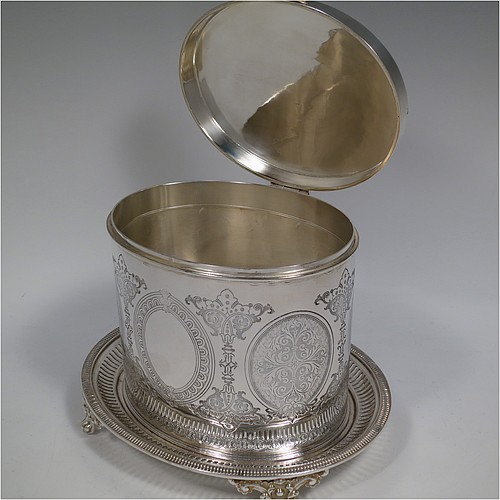 An Antique Victorian Silver Plated biscuit box, having an oval body with straight sides and very pretty hand-chased floral work, a hinged slightly domed lid with a thumb-piece, and all sitting on a hand-pierced attached plate with four cast foliate feet. Made by Roberts and Belk of Sheffield in ca. 1880. The dimensions of this fine hand-made antique silver-plated biscuit box are height 15 cms (6 inches), length 20 cms (8 inches), and width 17 cms (6.75 inches).    