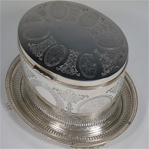 An Antique Victorian Silver Plated biscuit box, having an oval body with straight sides and very pretty hand-chased floral work, a hinged slightly domed lid with a thumb-piece, and all sitting on a hand-pierced attached plate with four cast foliate feet. Made by Roberts and Belk of Sheffield in ca. 1880. The dimensions of this fine hand-made antique silver-plated biscuit box are height 15 cms (6 inches), length 20 cms (8 inches), and width 17 cms (6.75 inches).    