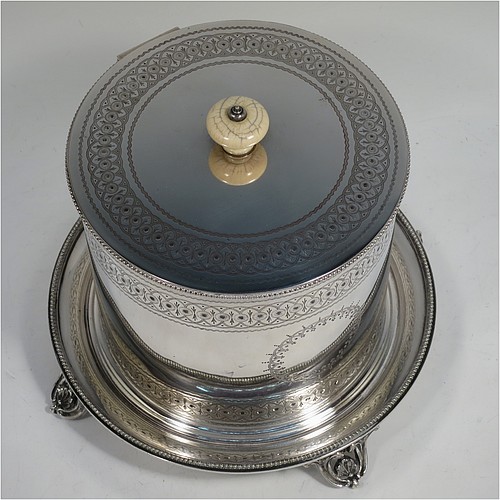 A very pretty Antique Victorian Silver Plated biscuit box, having a round body with straight sides and applied bead-edged borders, with very pretty hand-engraved bands of geometrical and floral work, a hinged flat lid with bone finial, and all sitting on an attached plate with four cast scroll and shell feet. Made by Elkington and Co., of Sheffield in ca. 1880. The dimensions of this fine hand-made antique silver-plated biscuit box are height 16 cms (6.3 inches), and diameter at base 18 cms (7 inches).