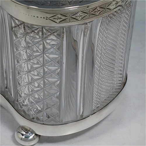 An Antique Victorian silver plated and cut crystal biscuit jar, having a hobnail and fluted cut crystal body, a hand-engraved mechanically double-hinged lid with a swing handle, and all sitting on a base with four cushion feet. Made by Thomas Wilkinson & Sons of Sheffield in ca. 1890. The dimensions of this fine hand-made antique silver-plated and hand-cut crystal biscuit jar are height inc. handle 23 cms (9 inches), length of base 19 cms (7.5 inches), and width of base 14 cms (5.5 inches).