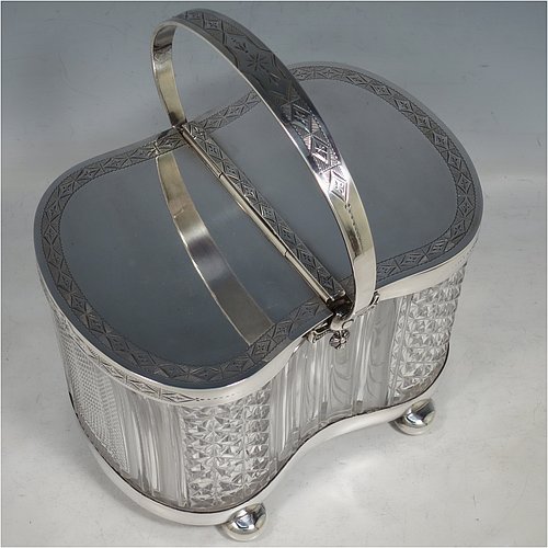 An Antique Victorian silver plated and cut crystal biscuit jar, having a hobnail and fluted cut crystal body, a hand-engraved mechanically double-hinged lid with a swing handle, and all sitting on a base with four cushion feet. Made by Thomas Wilkinson & Sons of Sheffield in ca. 1890. The dimensions of this fine hand-made antique silver-plated and hand-cut crystal biscuit jar are height inc. handle 23 cms (9 inches), length of base 19 cms (7.5 inches), and width of base 14 cms (5.5 inches).