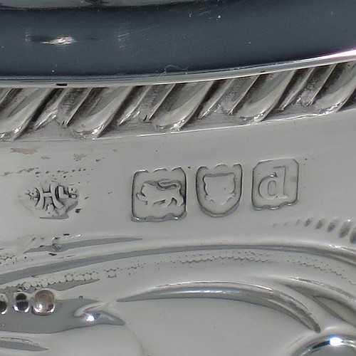 An Antique Victorian Sterling Silver biscuit box, having a round straight-sided body with hand-chased fluting and floral decoration, a hinged lid with cast foliate finial, and sitting on an attached base plate with a gadroon border and three cast foliate & lions-paw feet. Made by William Hutton & Sons of London in 1899. The dimensions of this fine hand-made antique silver biscuit box are height 18 cms (7 inches), diameter at base 19 cms (7.5 inches), and it weighs approx. 744g (24 troy ounces).