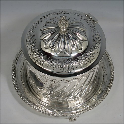 An Antique Victorian Sterling Silver biscuit box, having a round straight-sided body with hand-chased fluting and floral decoration, a hinged lid with cast foliate finial, and sitting on an attached base plate with a gadroon border and three cast foliate & lions-paw feet. Made by William Hutton & Sons of London in 1899. The dimensions of this fine hand-made antique silver biscuit box are height 18 cms (7 inches), diameter at base 19 cms (7.5 inches), and it weighs approx. 744g (24 troy ounces).