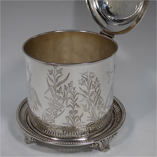 An Antique Victorian Silver Plated Chinoiserie style biscuit box, having a round body with straight sides and applied bead-edged borders, with very pretty hand-engraved flowers, reeds, birds, and butterfly work, a hinged domed lid with cast finial, and all sitting on a hand-pierced attached plate with four cast scroll feet. Made by the Atkin Brothers of Sheffield in ca. 1880. The dimensions of this fine hand-made antique silver-plated biscuit box are height 18 cms (7 inches), and diameter at base 17.5 cms (7 inches).    