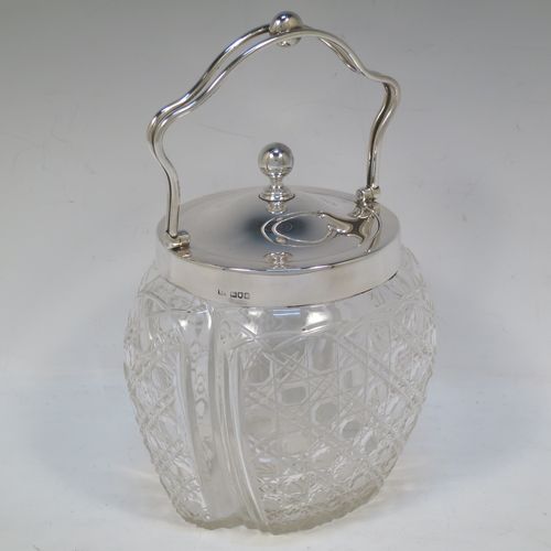 A pretty Antique Edwardian Sterling Silver and hand-cut crystal biscuit jar, having an unusual crystal body with hand-cut hobnail pattern panels with fluted corners, a plain round lift-off lid with a ball finial, a wire-work swing handle, and all sitting on a star-cut flat base. Made by Robert Pringle of London in 1904. The dimensions of this fine hand-made antique silver and crystal biscuit jar are height (excluding handle) 15 cms (6 inches), length 15 cms (6 inches), and width 13 cms (5 inches).  