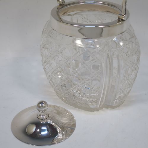 A pretty Antique Edwardian Sterling Silver and hand-cut crystal biscuit jar, having an unusual crystal body with hand-cut hobnail pattern panels with fluted corners, a plain round lift-off lid with a ball finial, a wire-work swing handle, and all sitting on a star-cut flat base. Made by Robert Pringle of London in 1904. The dimensions of this fine hand-made antique silver and crystal biscuit jar are height (excluding handle) 15 cms (6 inches), length 15 cms (6 inches), and width 13 cms (5 inches).