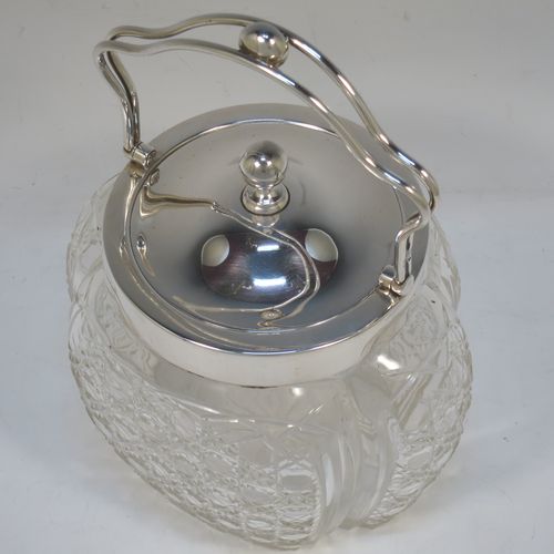 A pretty Antique Edwardian Sterling Silver and hand-cut crystal biscuit jar, having an unusual crystal body with hand-cut hobnail pattern panels with fluted corners, a plain round lift-off lid with a ball finial, a wire-work swing handle, and all sitting on a star-cut flat base. Made by Robert Pringle of London in 1904. The dimensions of this fine hand-made antique silver and crystal biscuit jar are height (excluding handle) 15 cms (6 inches), length 15 cms (6 inches), and width 13 cms (5 inches).