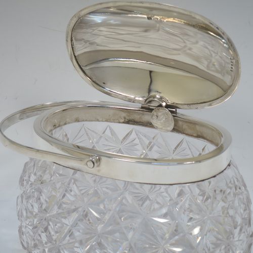 A very pretty and unusual Antique Victorian Sterling Silver and hand-cut crystal biscuit jar, having an oval crystal body with hand-cut hobnail and star-cut work, a plain oval mechanical lid which opens when moving the plain hinged swing-handle either left or right, and all sitting on a flat star-cut base. Made by Heath and Middleton of Birmingham in 1899. The dimensions of this fine hand-made antique silver and crystal biscuit jar are height (excluding handle) 13 cms (5 inches), length 16.5 cms (6.5 inches), and width 9 cms (3.5 inches).